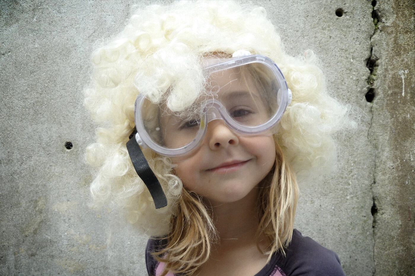 Stella as a kid, wearing a blonde curly wig and safety goggles