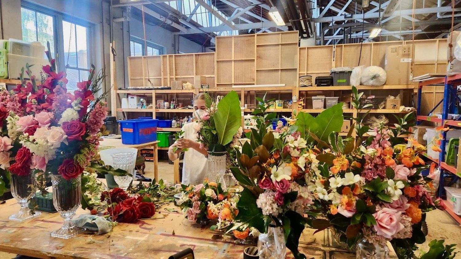 Stella arranging flowers among buckets of roses and native greenery in a floristry workshop