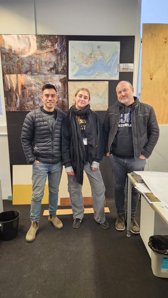 Stella standing with two colleagues in front of set design boards for The Artful Dodger