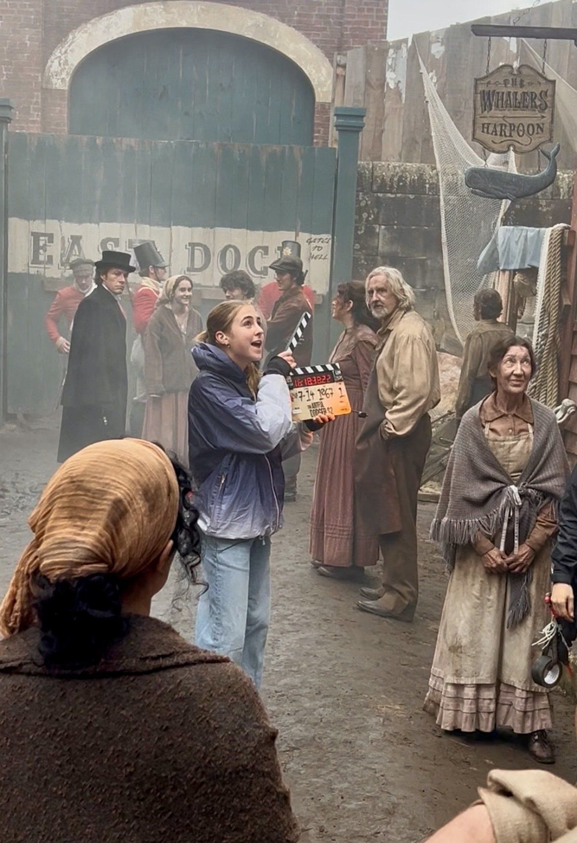 Stella holding a clapper board on the East Dock set of The Artful Dodger, surrounded by actors in period costume
