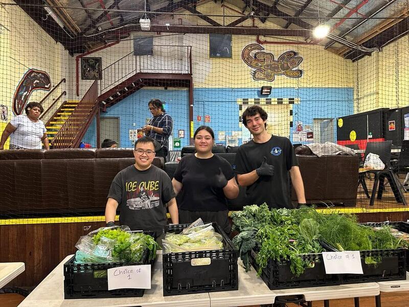 Three Food Circle volunteers giving a thumbs up in front of crates of vegetables