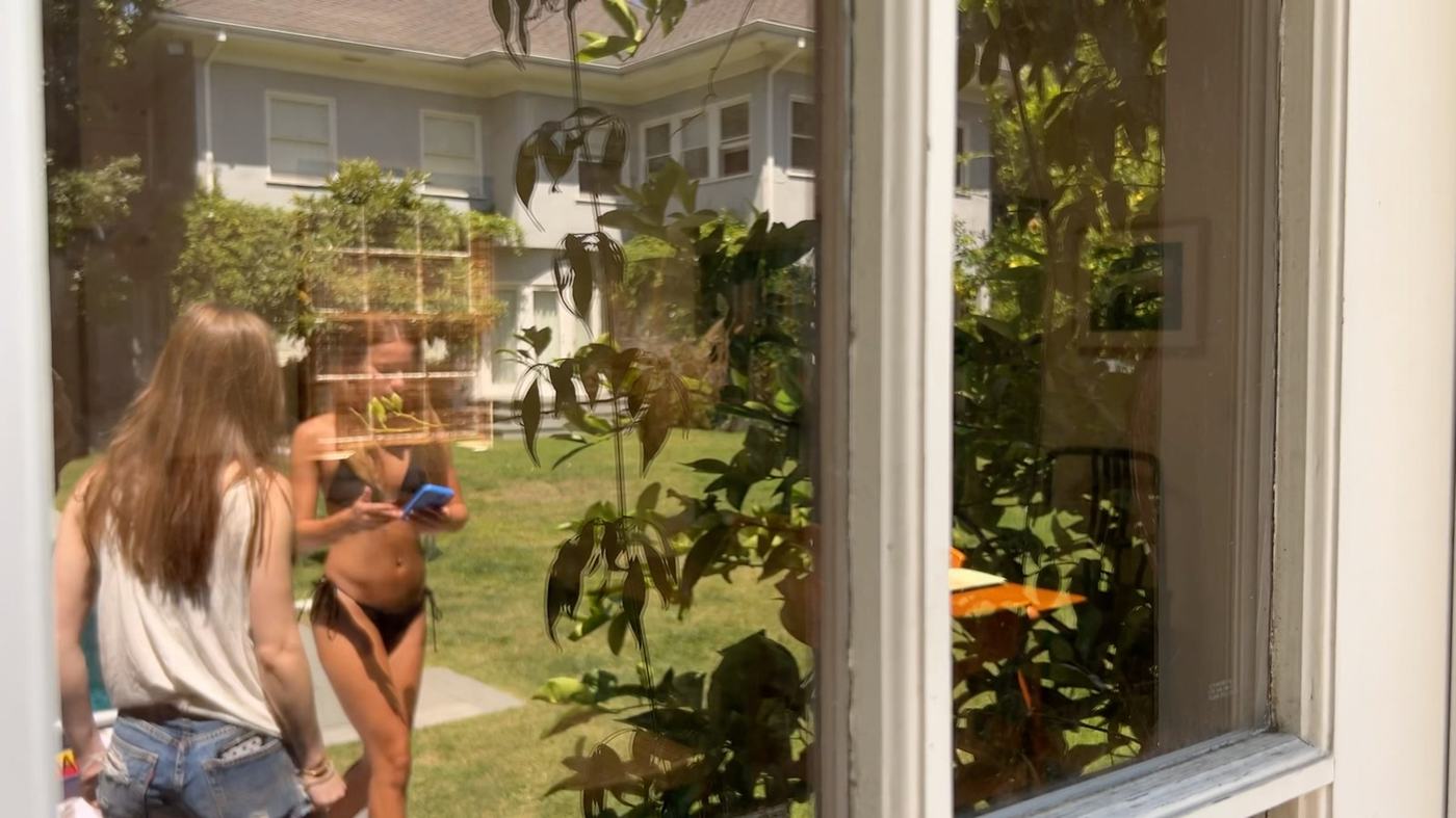 A girl by a pool looking at her phone with a friend nearby